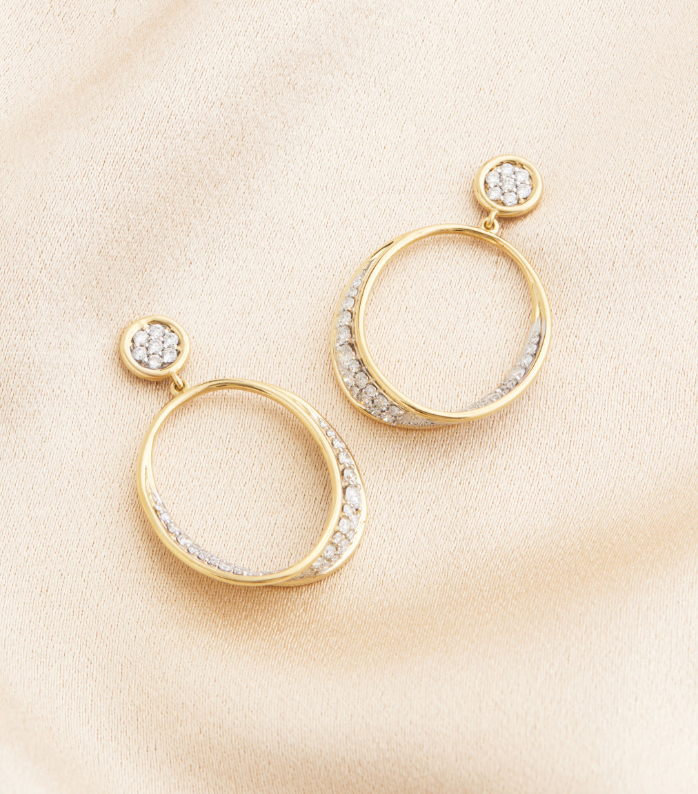 Gold hoop earrings with diamond accents on a beige fabric background