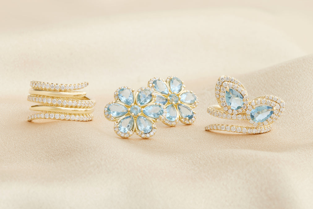 Three gold rings with blue gemstones on a beige background